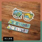 استیکر سفر و ماجراجویی فانتزی شامل استیکر عینک آفتابی ترکیبی کوه و ساحل دریا و استیکر کلمه Adventure با تم سبز و کرم مناسب برای تزیین وسایل سفر و لپ‌تاپ.