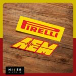 مجموعه دو عددی استیکر خودرو شامل یک استیکر مستطیلی زرد رنگ با نوشته قرمز برند تایر سازی Pirelli و یک استیکر با حروف کج زرد و حاشیه قرمز برند قطعات تیونینگ AEM به همراه نماد خط ضربان قلب یا فرکانس در میان آن.
